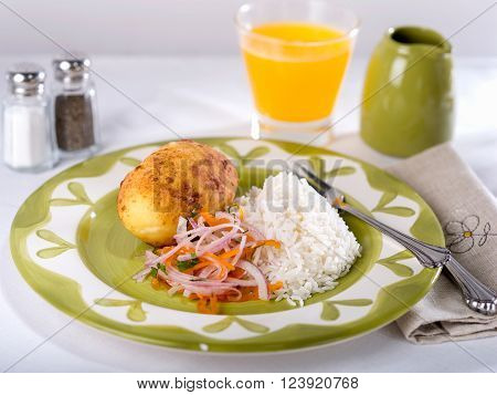 Papa Rellena, a fried potato stuffed with meat filling, a typical Peruvian dish garnished with onion salsa on white and green plate.