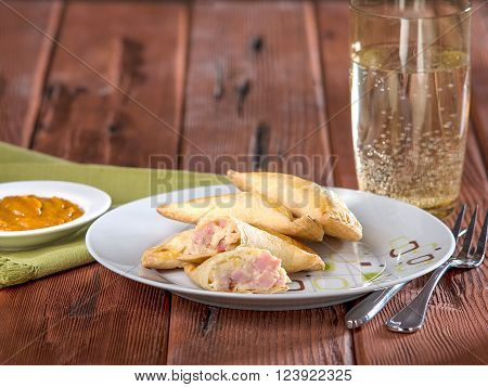 Ham and cheese empanadas, empanadas mixtas, a typical Peruvian dish served on white plate on wooden table top.