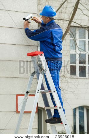 Male Technician Standing On Stepladder Fitting Cctv Camera
