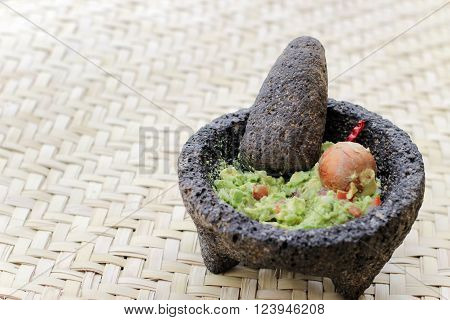 Photograph of smashed avocado guacamole in a traditional stone molcajete