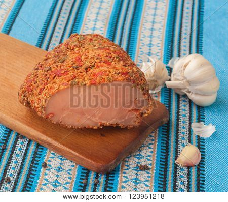 A piece of meat balyk with a crust of spices and sesame seeds on a cutting board
