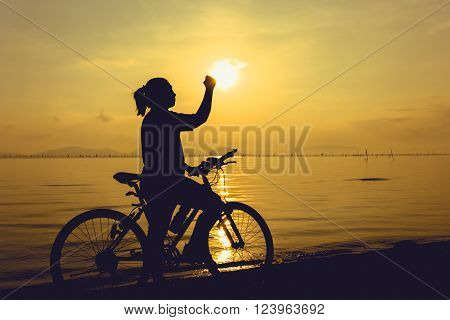 Silhouette of happy female with mountain-bike on colorful yellow sky background. Active outdoors lifestyle for healthy concept. Action of winner or successful people.
