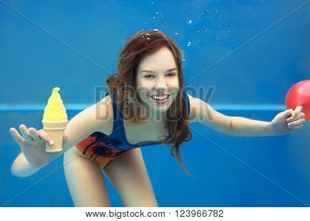Beautiful smiling red hair girl eating yellow ice cream in the swimming pool underwater in summer