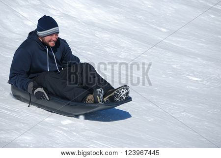 Man in toboggan on a sled on a snowhill going down laughing with copyspace.