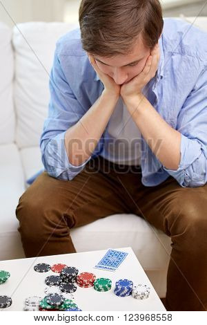 game, gambling and fail concept - losing man with playing cards and chips on table at home
