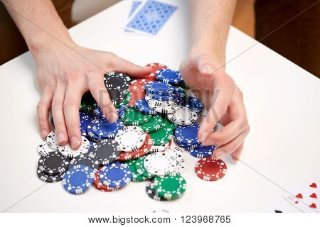 leisure, games, gambling and entertainment - close up of male hands with casino chips and playing cards making bet or taking win at home
