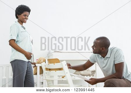 Pregnant woman looking at man fixing a baby chair at home