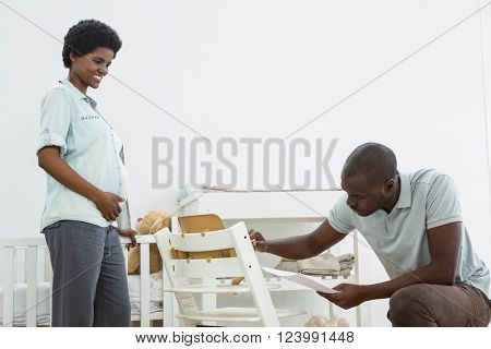 Pregnant woman looking at man fixing a baby chair at home