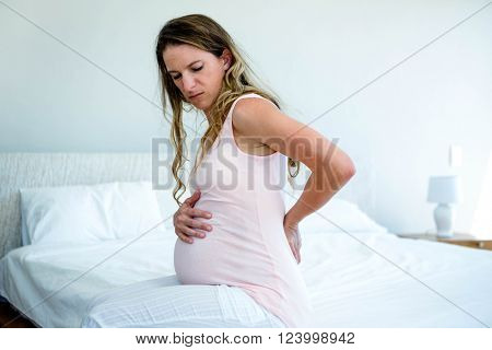 sad pregnant woman, sitting on a bed, with back pain