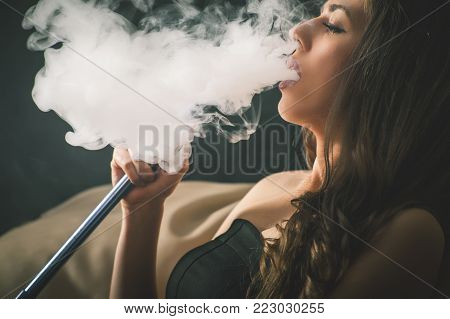Closeup Young, beautiful girl smoke a hookah at club. Sexy woman smoking. Fashion
