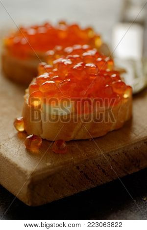 Sandwiches with red caviar on the wooden cutting board. Home made food. In front of light background.