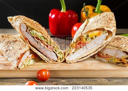 Shawarma chicken roll in a pita with fresh vegetables and cream sauce on wooden background. Selective focus.