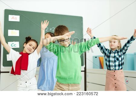 Cute schoolkids in casua lwear dancing after lesson in classroom while enjoying break