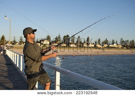 young attractive and happy man in shirt and hat fishing at beach sea dock using fish road enjoying weekend hobby in holidays and relaxing tourism concept