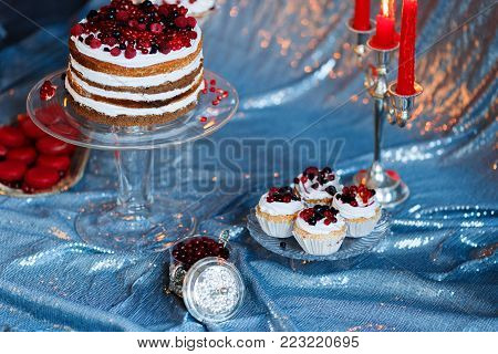 Sweet bar with muffins cakes, sweets, fruits and candle holders in area of wedding party on a silver background.