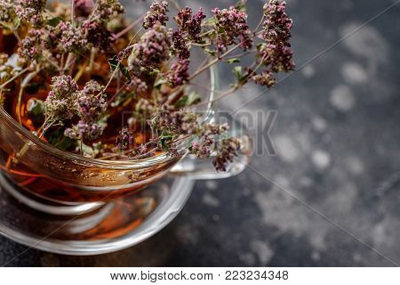Herbal tea in a glass cup with dry marjoram on a dark background.Close up.