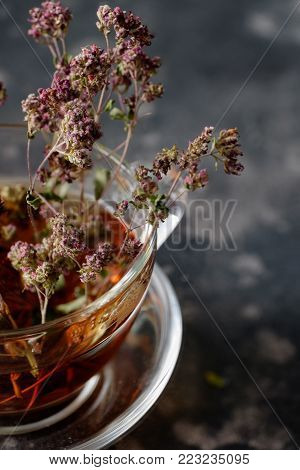 Herbal tea in a glass cup with dry marjoram on a dark background.Close up. Vertical.