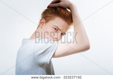 Emotional struggle. Earnest pleasant young guy looking at the camera while wearing t shirt and touching hair
