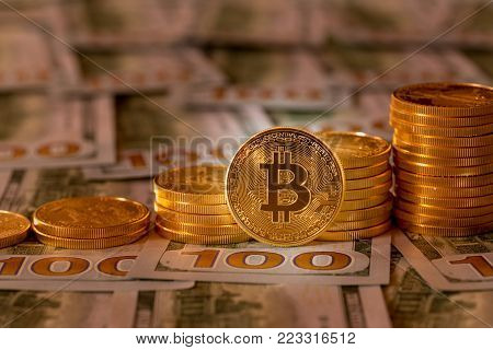 Stack of golden on new design of US currency one hundred dollar bills with spotlight on the Bitcoin in the foreground