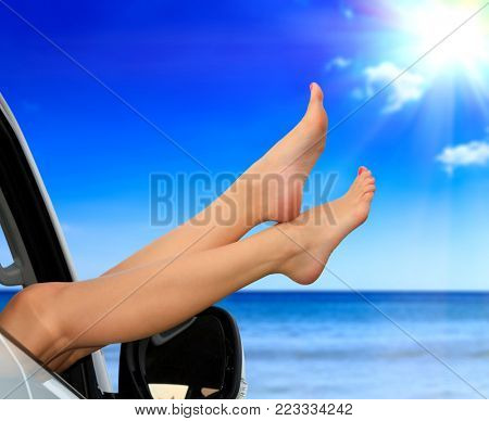 Beaitiful female legs against the sea and summer blue sky. Vacation, travel summer holidays concept. Woman shows her slim legs from the car window