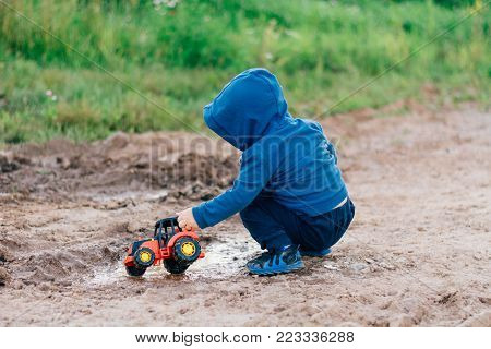 the boy in the blue suit covered in mud plays with a toy car in the dirt