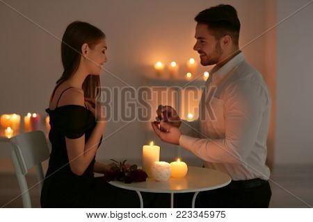 Young man with engagement ring making proposal to his girlfriend while sitting at table with burning candles