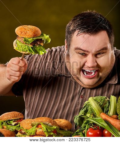 Fat man eating fast food hamberger. Breakfast for overweight person. Junk meal leads to obesity. Person regularly overeats concept on green background. Unhealthy food processing eating.