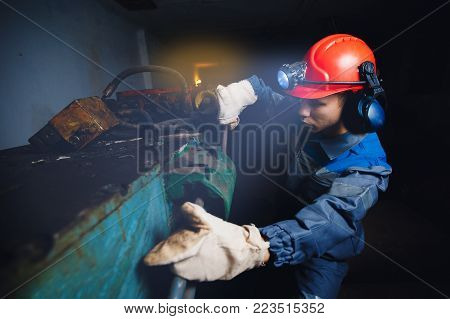 young miner man underground in a mine for coal mining in overalls is busy with work, repairing against the backdrop of mining equipment. Portrait.