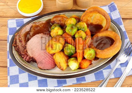 Traditional English roast beef meal with roasted potatoes, vegetables and Yorkshire puddings