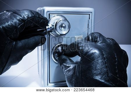 Close-up Of A Thief's Hand Using Stethoscope While Unlocking Safe