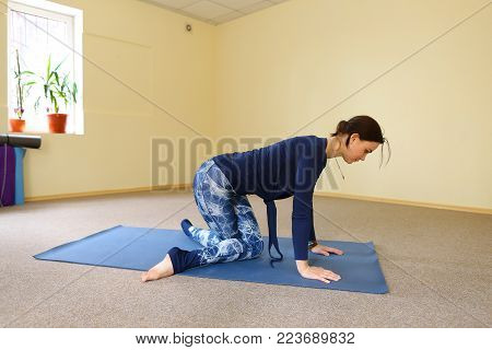 Sportswoman focused on stretch before Pilates class. Girl doing warm up for legs on mat. Female has hair pulled back, concentrated look. Athlete dressed in dark top, yoga legging trains in fitness room. Concept of online training, customizable workouts.