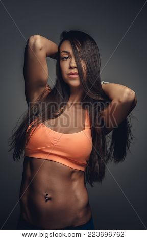 Awesome athletic woman with long dark hair in an orange sports bra isolated on agrey background.