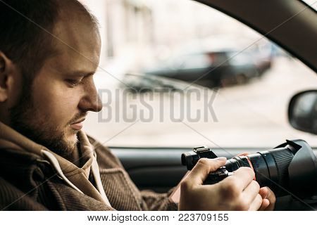 Investigator or private detective or reporter or paparazzi sitting in car and taking photo with professional camera, toned