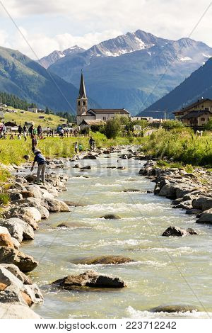 Livigno, Italy - August 1: People Around Spol River With Church Of Santa Maria In Background On 1 Au