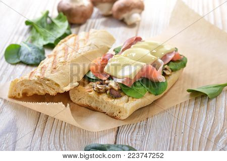 Street food: Hot Panini with Spanish Serrano ham and young spinach leaves topped with grated cheese served on a wooden background