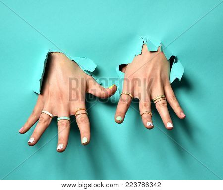 Beautiful woman hands with yellow pink white pattern nail polish and silver stacking rings and bracelets on a mint background