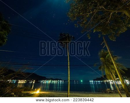 stars at nightsky with palmtrees and campfire near village