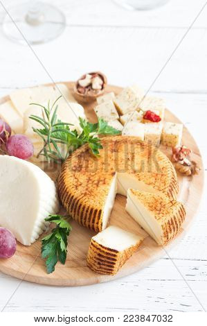 Cheese platter with assorted cheeses, grapes, nuts over white wooden background, copy space. Italian cheese and fruit platter.