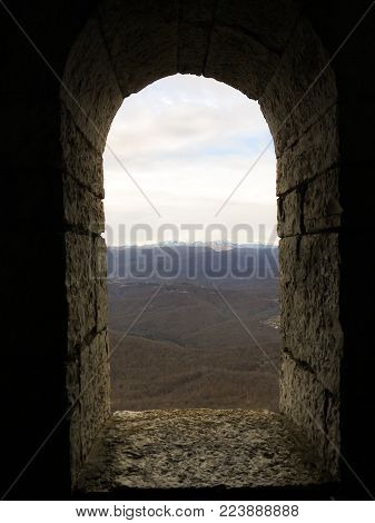 old stone window in the form of an arch with a view of the mountains 1