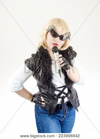 A semi-long portrait of a female rock musician in a black leather jacket and gloves on a gray background. The concept of music and rock style