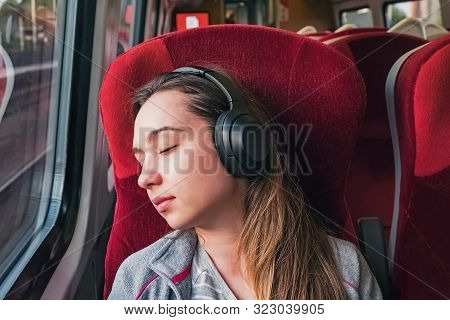 Young Woman Relaxing Or Sleeping While Listening Music In Headphones Sitting Near The Window In Trai