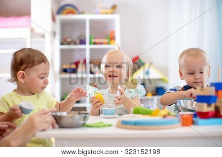 Babies Playing Together In Kindergarten Or Creche. Kids Sitting At Table In Nursery Or Daycare
