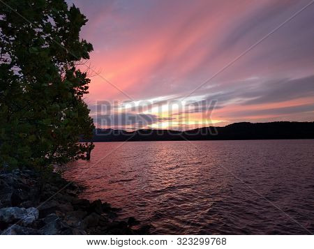 Vibrant sky with shades of purple and red strongly reflecting off a lake, viewed from the shore overlooking some hills