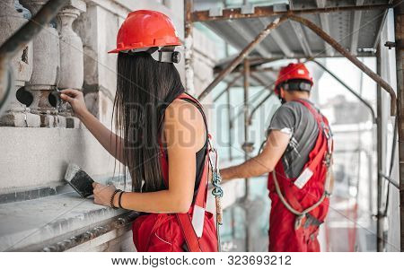 Two Workers Standing On Scaffolding, Perform Work On The Restoration Of The Facade Of The Old Buildi