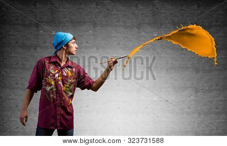 Young Artist Painting Orange Brush Stroke. Male Painter In Dirty Shirt And Bandana With Paintbrush O