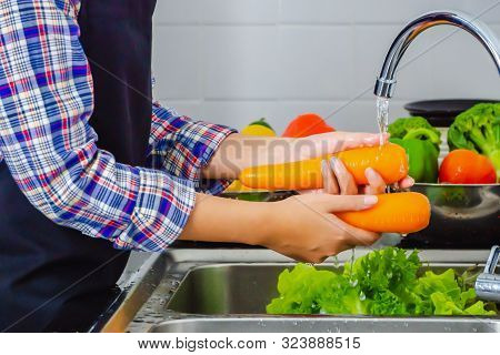 Young Woman Washing Carrot To Remove Pesticides Before Cooking In Kitchen. Fruit And Vegetables Wash