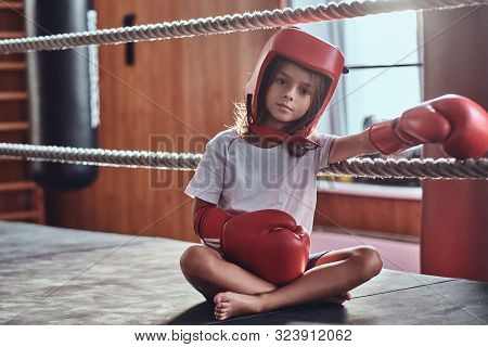 Sportive Young Girl Is Sitting On Sunny Ring Wearing Her Eguipment - Helmet And Boxing Gloves.