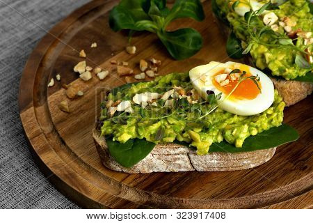 Avocado Toast With Soft Boiled Egg, Herbs, Spinach And Nuts On A Wooden Board. Healthy Breakfast