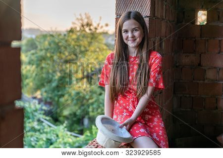 Beautiful Red Head Gir In Red Dress Sitting In The Wndow Of An Unfinished House Holding Hat In Hands