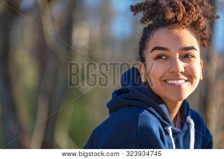 Outdoor portrait of beautiful happy mixed race biracial African American girl teenager female young woman smiling with perfect teeth wearing a blue hoodie